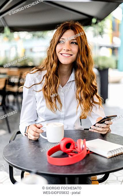 Young businesswoman sitting in cafe, using smartphone