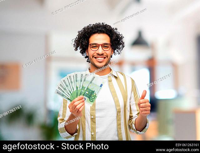 happy man with money showing thumbs up at office