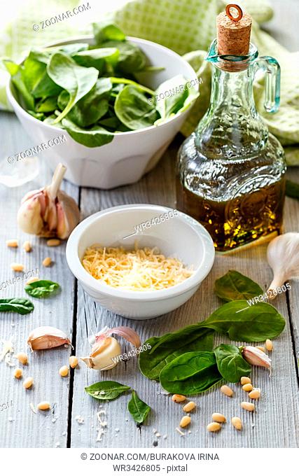 Products for making homemade pesto: spinach leaves, grated cheese, garlic, pine nuts, olive oil and blender on white wooden background