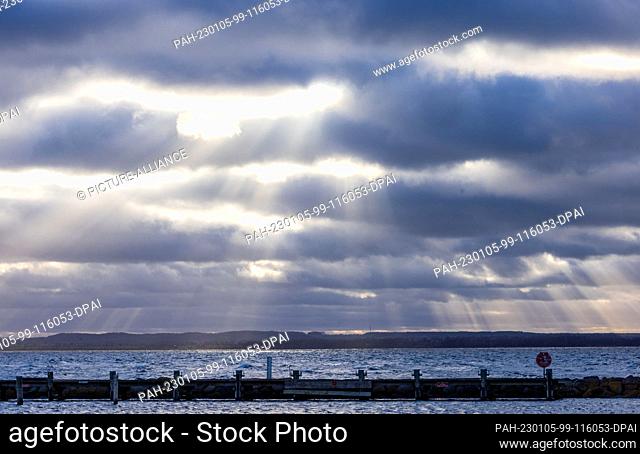 05 January 2023, Mecklenburg-Western Pomerania, Timmendorf (poel): The small pier with moorings for pleasure boats is seen in the backlight of the animal sun in...
