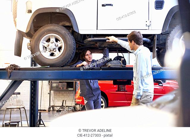 Mechanic under car talking to customer in auto repair shop