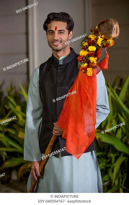 Smiling maharashtrian man in traditional dress holding the gudi while celebrating gudi padwa festival