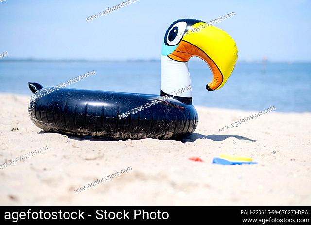 15 June 2022, Lower Saxony, Hooksiel: An inflatable floating animal in the shape of a toucan lies in the sand on the North Sea beach