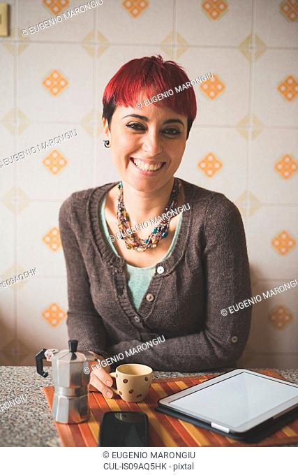 Portrait of young woman sitting at table, drinking coffee