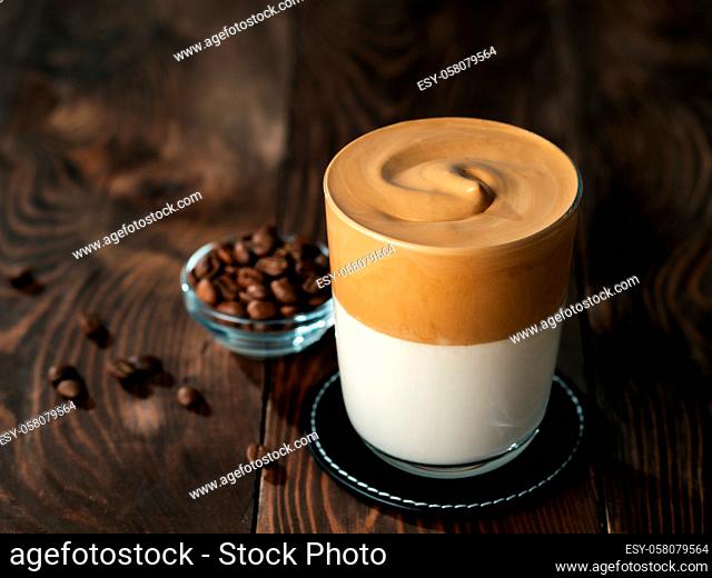 Trendy korean drink - dalgona coffee. Glass jar with cold or hot beverage - whipped instant coffee with milk and coffee beans on brown wooden background with...