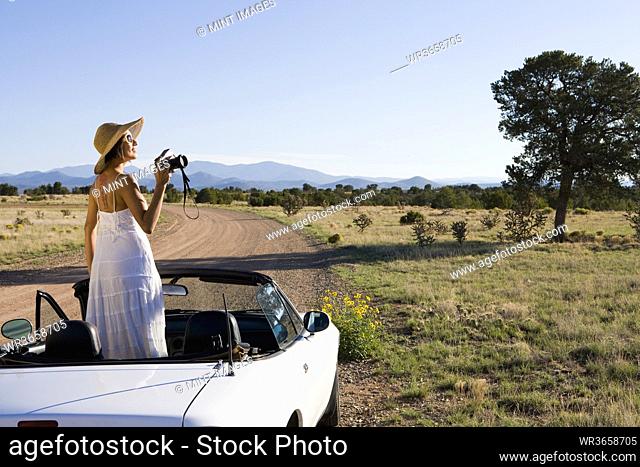 Native American woman in sun dress driving a white convertible sports car on desert dirt road