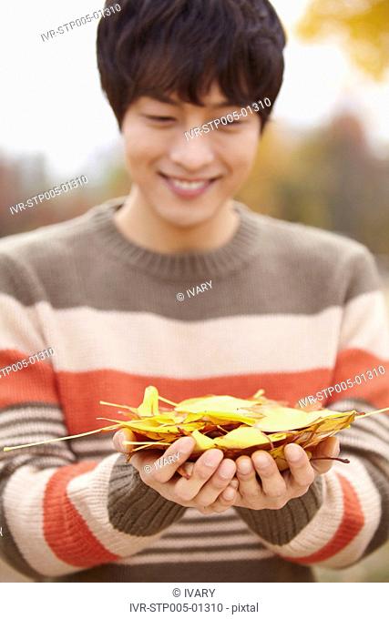 Young Man Holding Autumn Leaf In Park