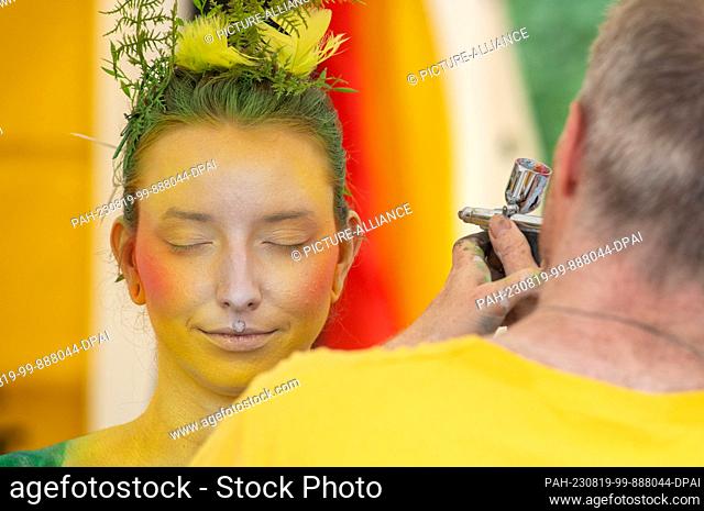 19 August 2023, Mecklenburg-Western Pomerania, Heringsdorf: Body painting artist Torsten Winter paints a model at the Bodypainting Festival in the seaside...