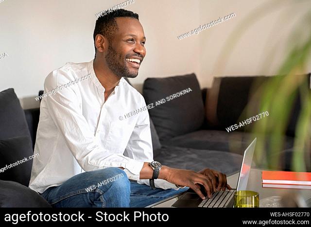 Portrait of laughing man sitting on couch using laptop