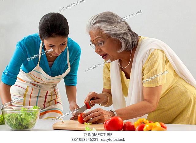 Woman teaching granddaughter how to cut tomato