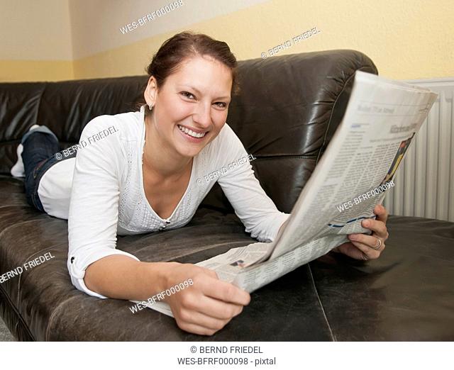 Germany, Brandenburg, Young woman reading newspaper
