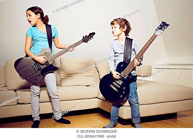 Boy and girl in lounge playing guitars looking away