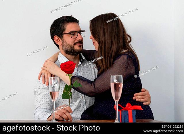 girl sitting on her husband's lap on valentine's day with champagne glasses and a rose