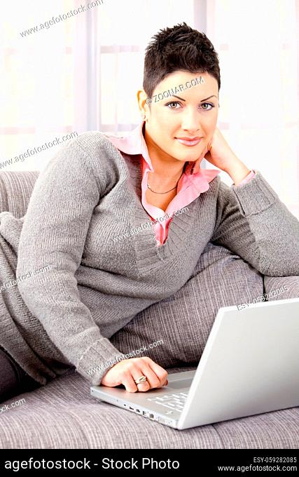 Woman sitting on sofa at home working on laptop computer