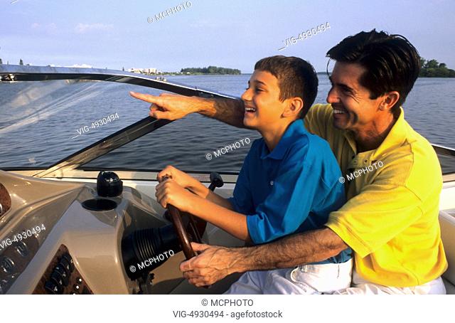 Hispanic father and son sharing the fun of boating and driving the boat together laughing and relaxing a fathers love - 01/01/2014
