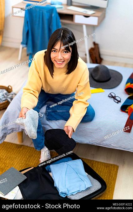 Smiling young woman packing luggage in bedroom