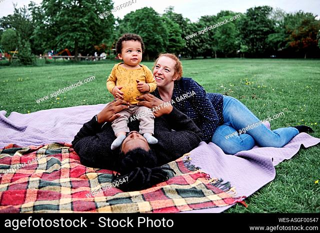 Happy family relaxing with son while lying on picnic blanket at park