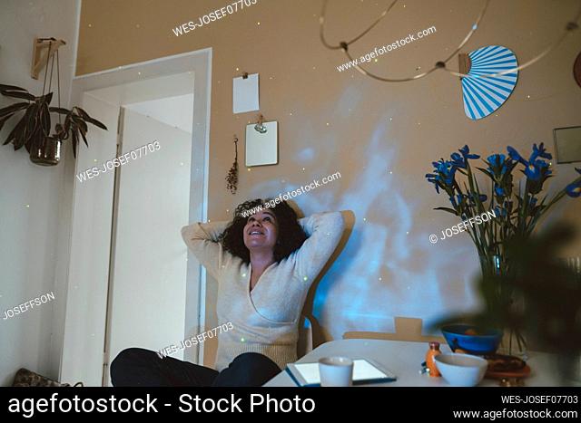 Smiling woman with hands behind head looking at astro light effects in room