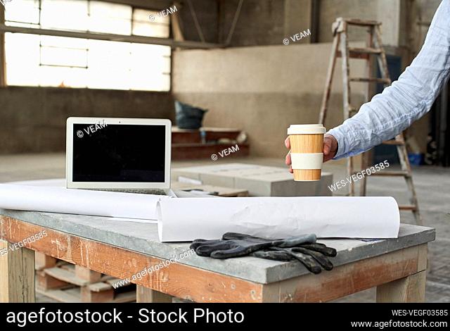 Hand of male architect placing coffee cup on table in building