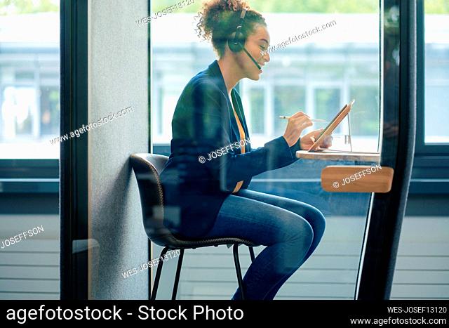 Businesswoman using tablet PC sitting in soundproof cabin at workplace