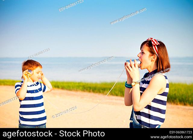 Kids having a phone call with tin cans on sea background