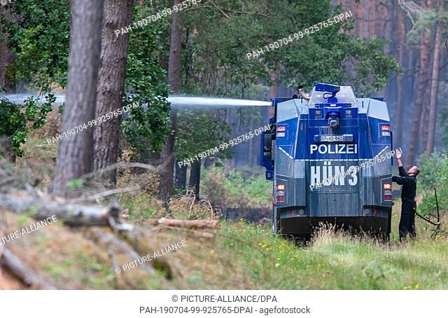 04 July 2019, Mecklenburg-Western Pomerania, Alt Jabel: A water cannon of the Federal Police splashes extinguishing water into a burnt down forest with glowing...