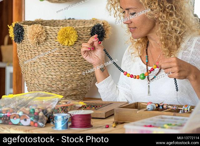 Young adult woman produce beads jewels at home at the table - modern home work with beads and cheaper jewelry - online store concept with creative people