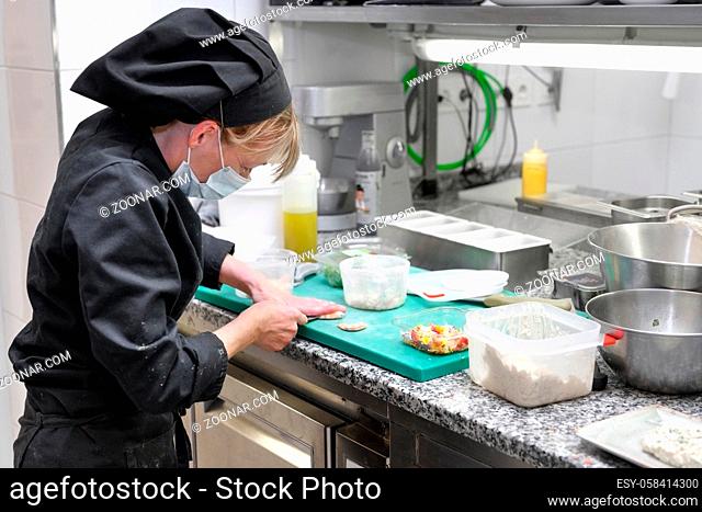 Woman Chef in protective face mask prepare food in the kitchen of a restaurant or hotel. Coronavirus prevention concept. High quality photo