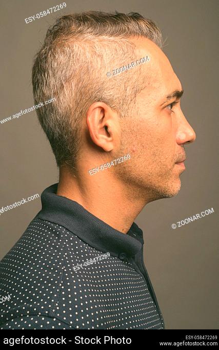 Studio shot of handsome Persian man with gray hair wearing blue polo shirt against gray background