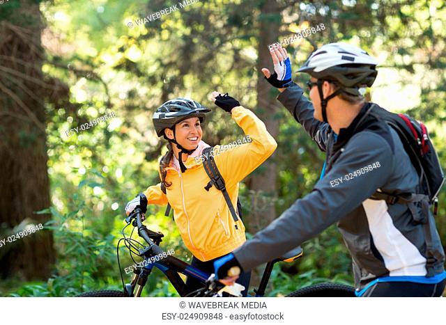 Biker couple giving high five while riding bicycle in the forest