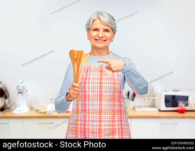smiling senior woman in apron with wooden spoons