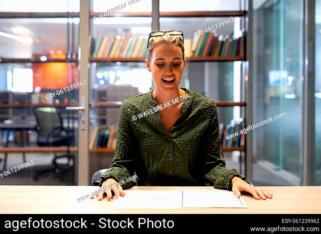 Smiling caucasian businesswoman sitting with agreement documents at desk in modern workplace