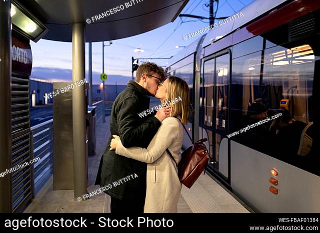 Kissing young couple standing at tram stop in the evening