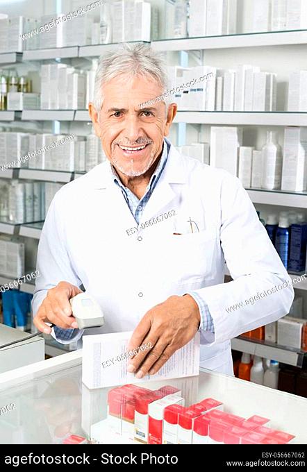 Portrait of senior male chemist scanning barcode on medicine box in pharmacy