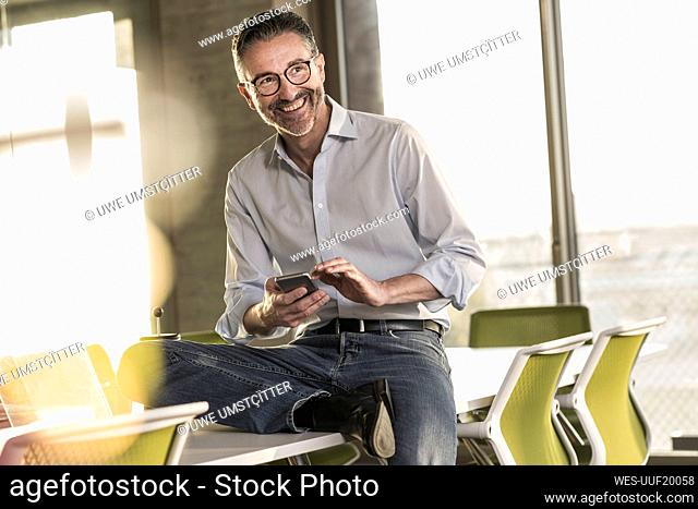 Happy mature businessman with cell phone in office