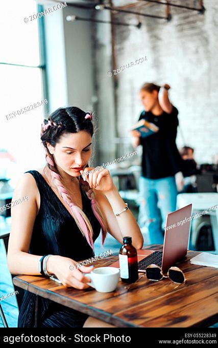 Young woman sitting in coffee shop at wooden table. On table is laptop