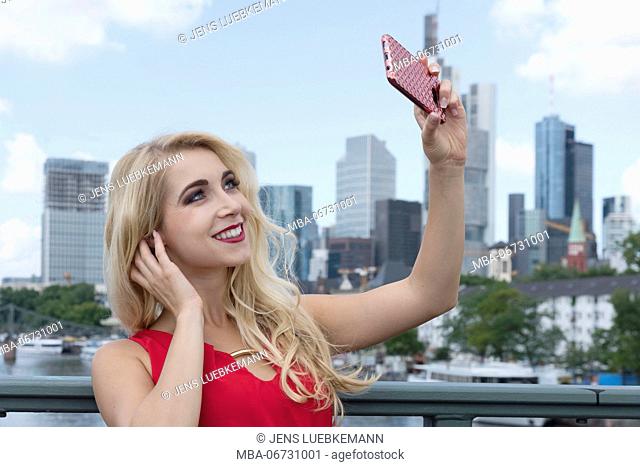 Young woman makes Selfie in front of skyline, Frankfurt, Hessen, Germany