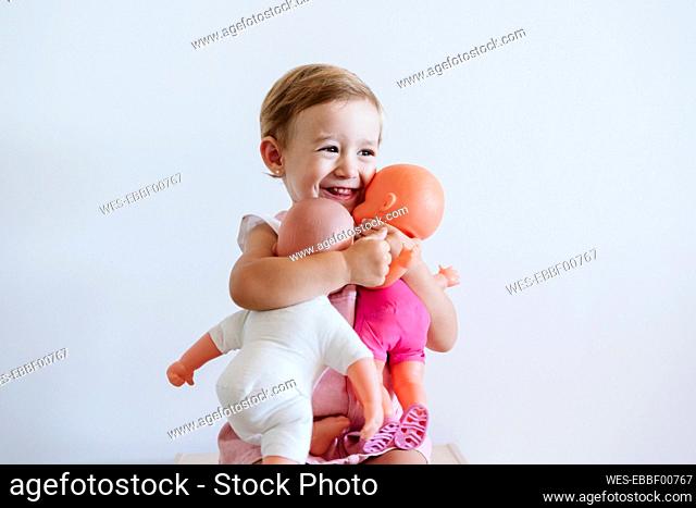 Baby girl embracing toys while sitting against wall