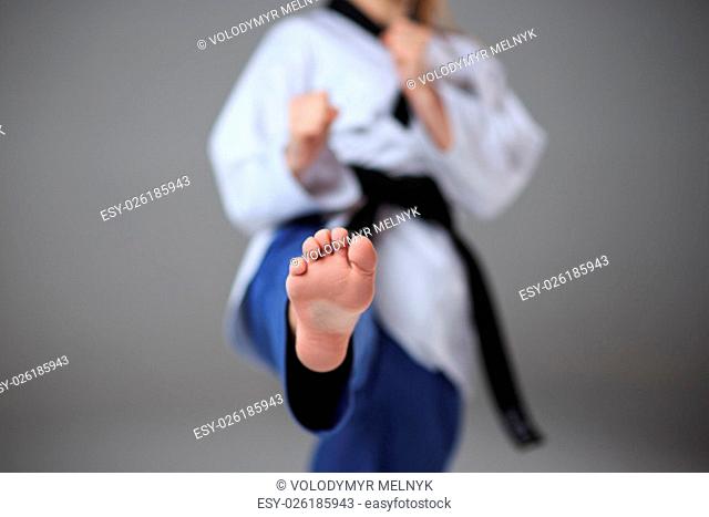 The foot of karate girl in white kimono and black belt training karate over gray background