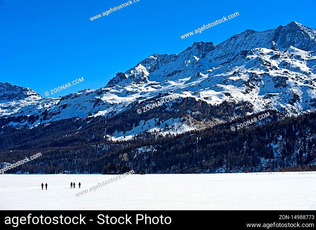 Fussgänger überqueren den zugefrorenen Silsersee, Corvatsch Massiv hinten, Sils im Engadin, Graubünden, Schweiz / Pedestrians crossing the frozen Lake Sils