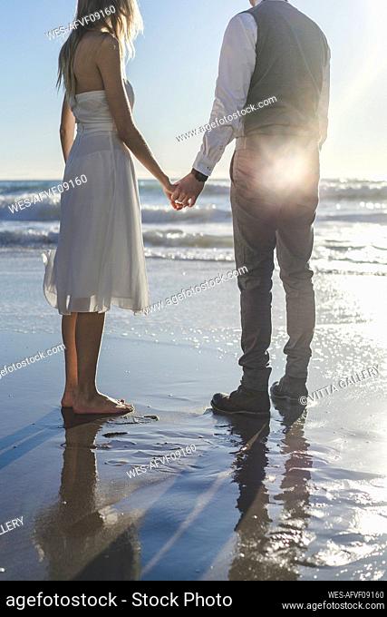 Young couple holding hands while standing on beach