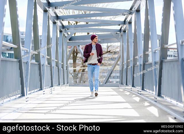 Young man walking on a bridge with earbuds and smartphone