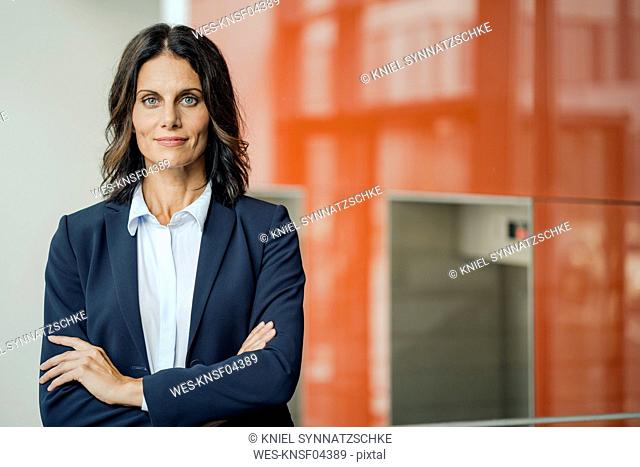 Portrait of a successful businesswoman, standing in front of elevator, with arms crossed