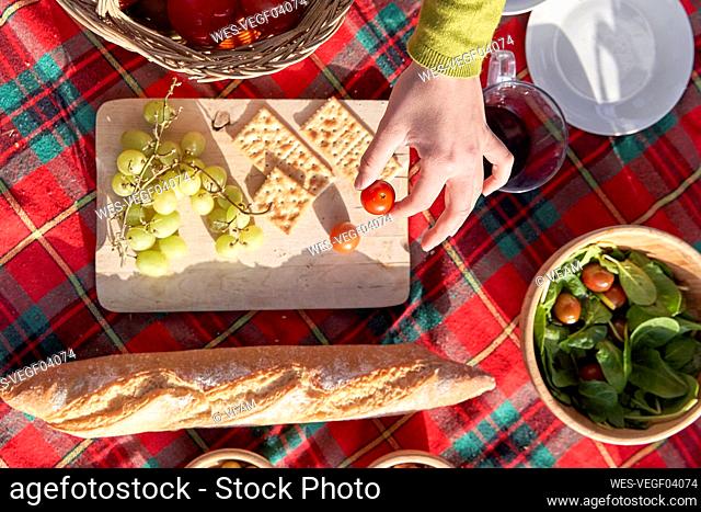 Woman holding cherry tomatoes over serving board on picnic blanket