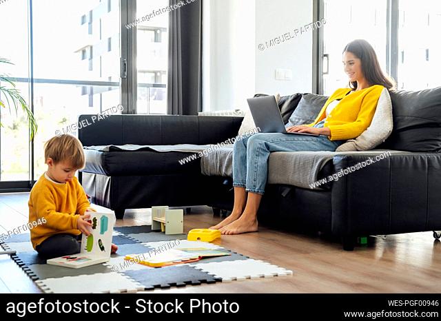 Mother working on laptop with baby boy playing at home