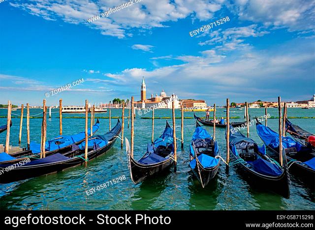 VENICE, ITALY - JUNE 27, 2018: Gondolas and gondolier in lagoon of Venice by Saint Mark (San Marco) square with San Giorgio di Maggiore church in background in...
