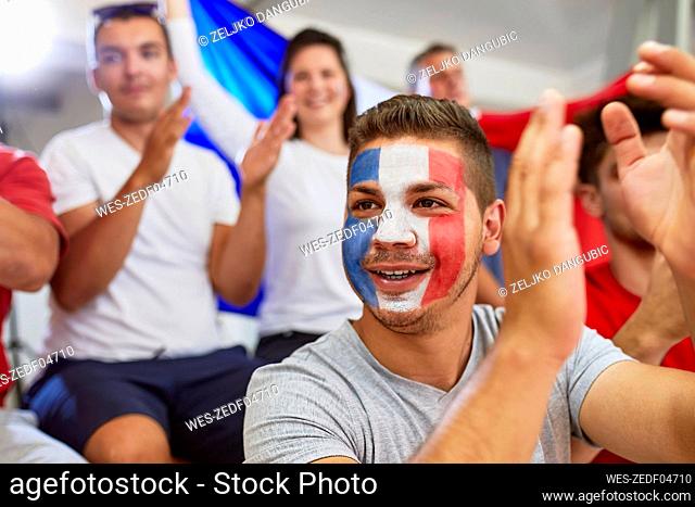 Contemplative man with French Flag painted on face clapping with fans in stadium