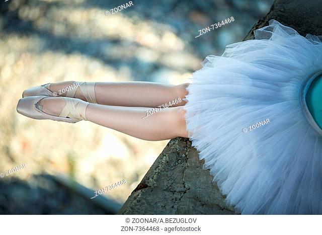 Ballerina sitting on the edge of the bridge. Feet shod with pointe. Dancer wearing a white tutu and blue swimsuit