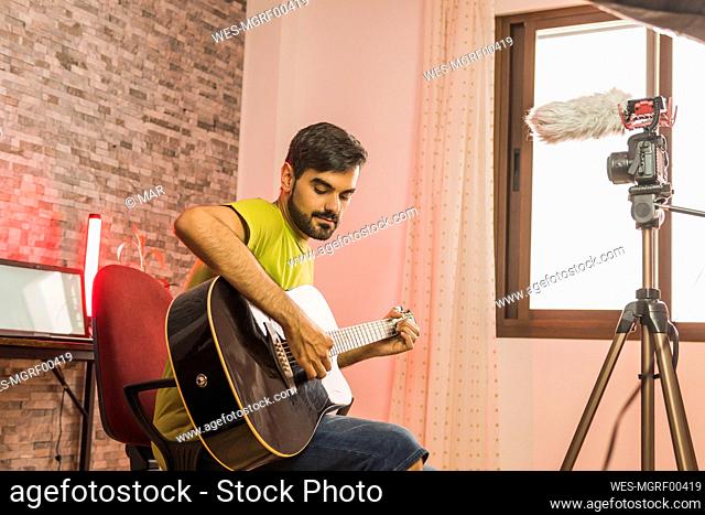 Male influncer filming in camera while playing guitar at home