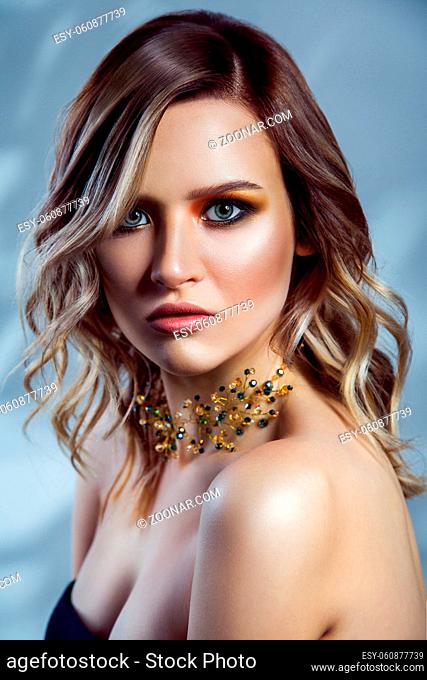 Beauty portrait of beautiful fashion model with makeup, colored wavy hairstyle and accessories on her neck. studio shot on blue background.